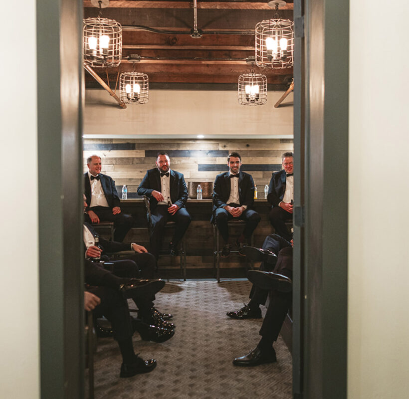 Groomsmen sitting on wooden benches in the grooms wedding suite