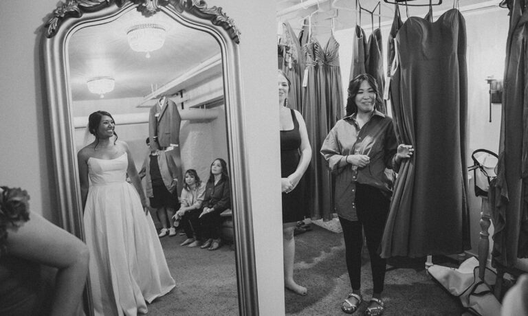 Black and white photo of a bride putting on her wedding dress in front of a mirror