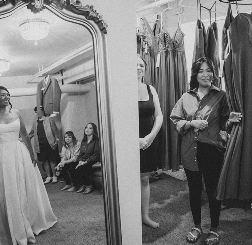 Black and white photo of a bride putting on her wedding dress in front of a mirror