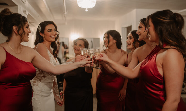 A bride and her bridesmaids in red dresses clinking Champaign glasses