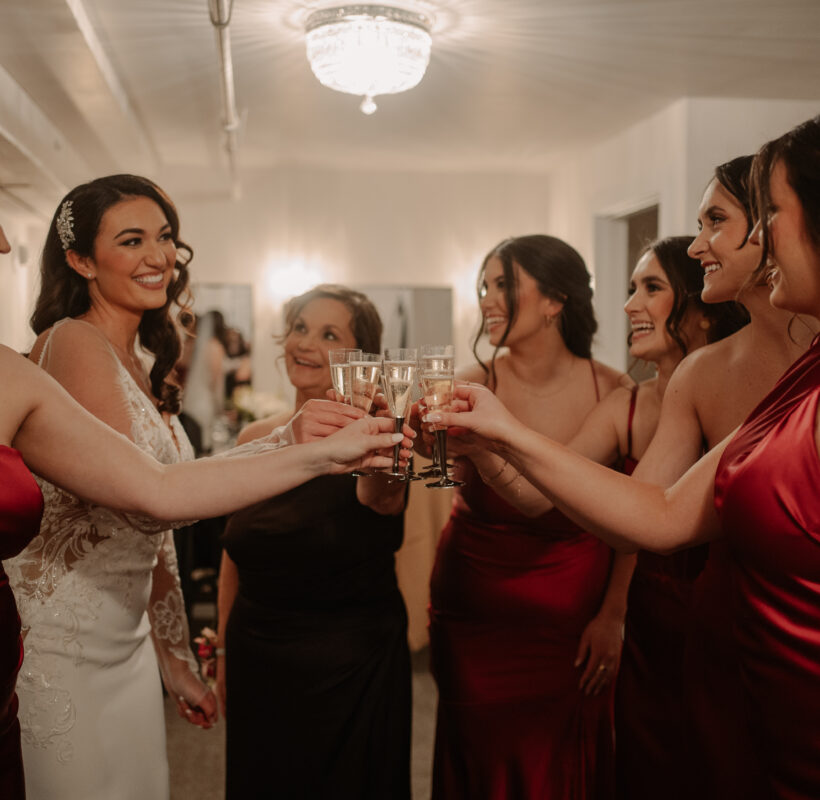 A bride and her bridesmaids in red dresses clinking Champaign glasses